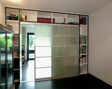 Raumteiler mit Milchglas-Gleittür in einer weißen Regalwand