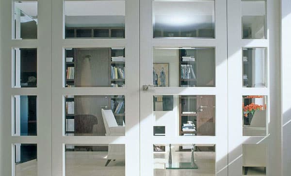 Weiße Flügeltür mit vielen Glasfeldern vor Bücherregal und Treppenaufgang