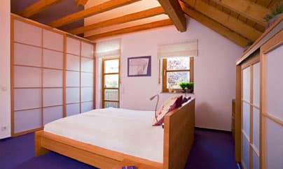 Schlafzimmer unterm Dach mit freistehendem Massivholzbett und Einbauschränken mit Japan-Gleittüren