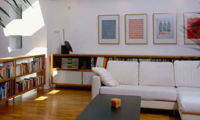 Wohnzimmer mit langem Bücherregal, Sideboard aus Massivholz und heller Couchlandschaft