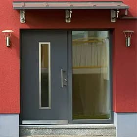 Anthrazitfarbene Haustür mit schmalem Glasstreifen an roter Fassade