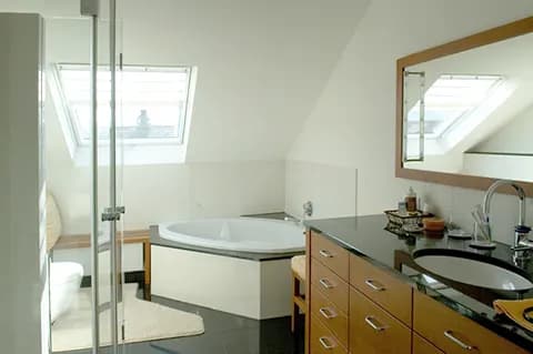 Badezimmer unterm Dach mit Eckbadewanne, Glasdusche und Waschtisch aus Holz