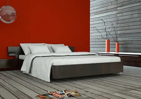 Schlafzimmer mit roter Akzentwand, Holzdielen und Steinwand hinter dem Bett